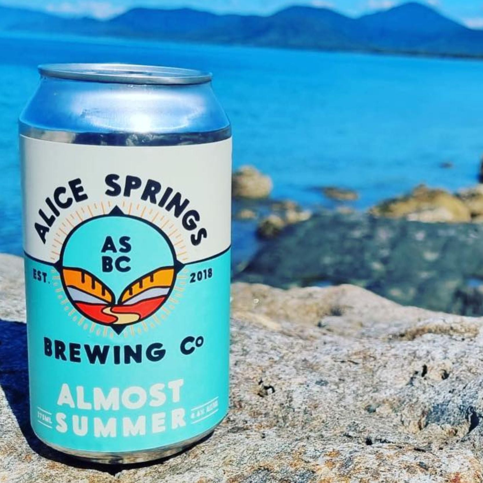can of alice springs brewing co almost summer pale ale with a lake in the background